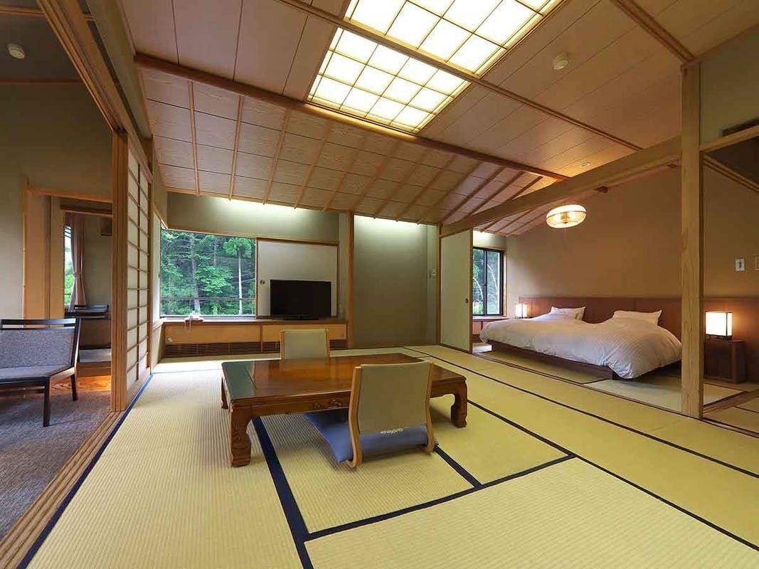 A traditional Japanese-style room with tatami flooring, a low table, a bed, and a television.