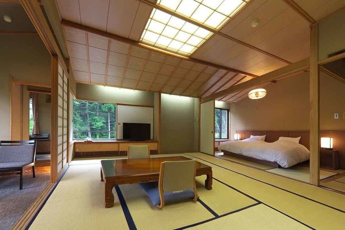 Une pièce de style japonais traditionnel, avec un sol recouvert de tatamis, une table basse, un lit et un téléviseur.