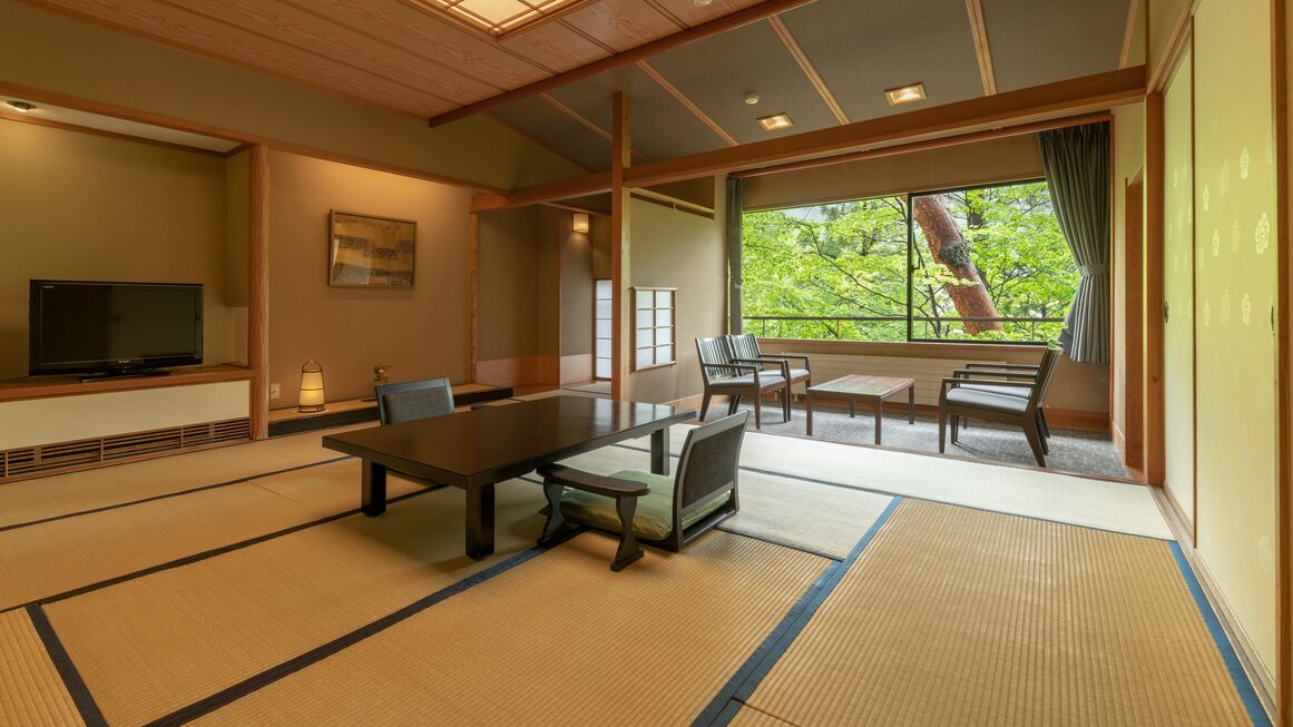 A traditional Japanese-style room with tatami flooring, a low table, chairs, a television, and a large window with a view of trees.