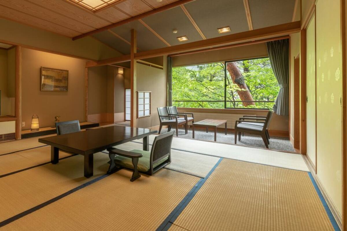 Une pièce de style japonais traditionnel, avec un sol recouvert de tatamis, une table basse, des chaises, un téléviseur et une grande fenêtre donnant sur la forêt.