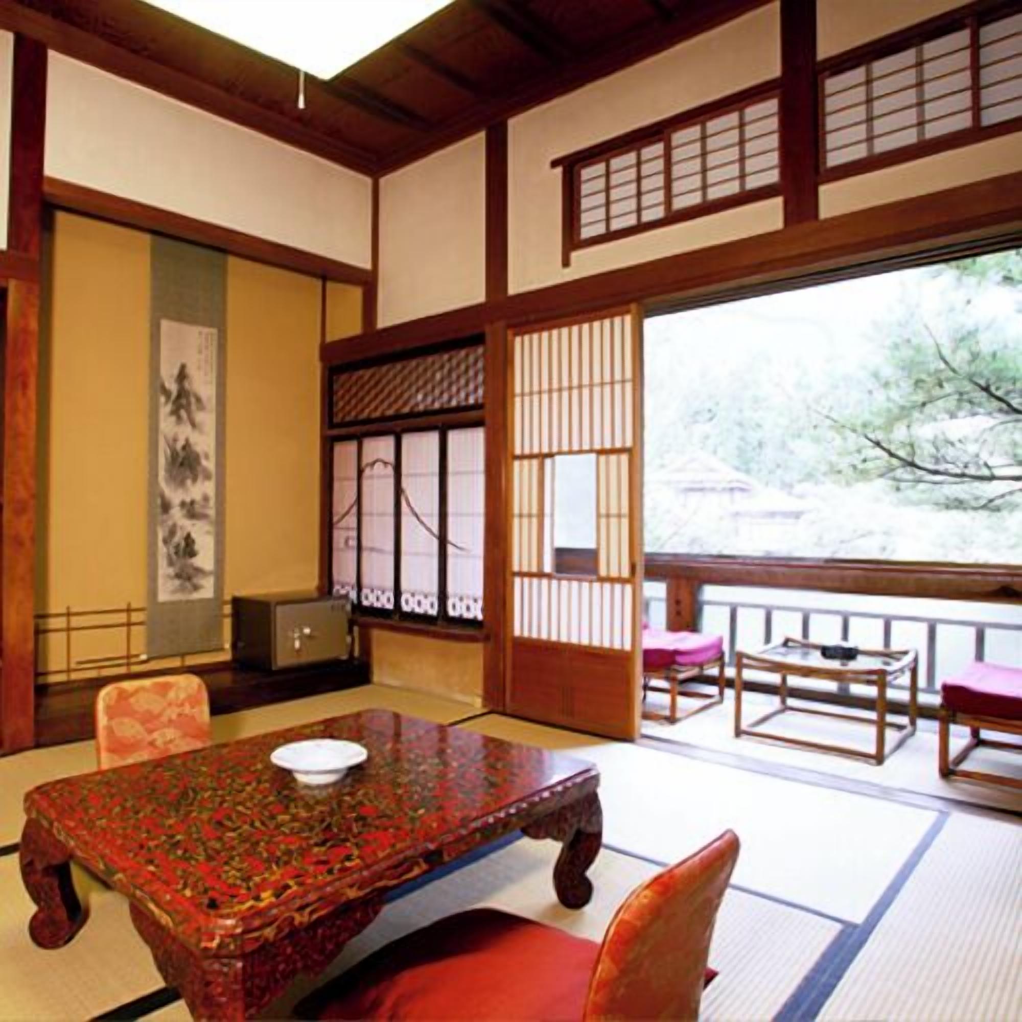 A traditional Japanese room with tatami flooring, a low table with a bowl, a wooden chair, and a sliding door with a view of a snowy landscape.