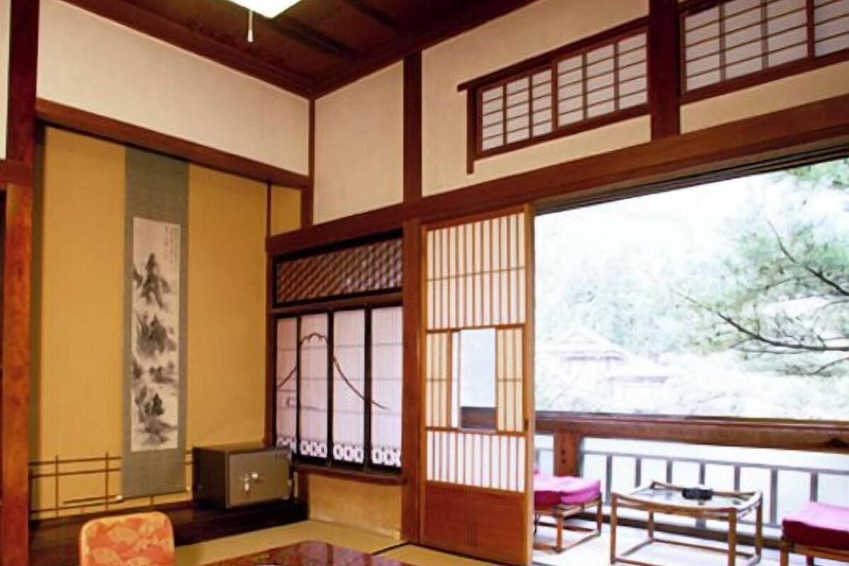Une pièce de style japonais traditionnel, avec un sol recouvert de tatamis, une petite table sur laquelle est posé un bol, une chaise en bois et une porte coulissante donnant sur un paysage enneigé.