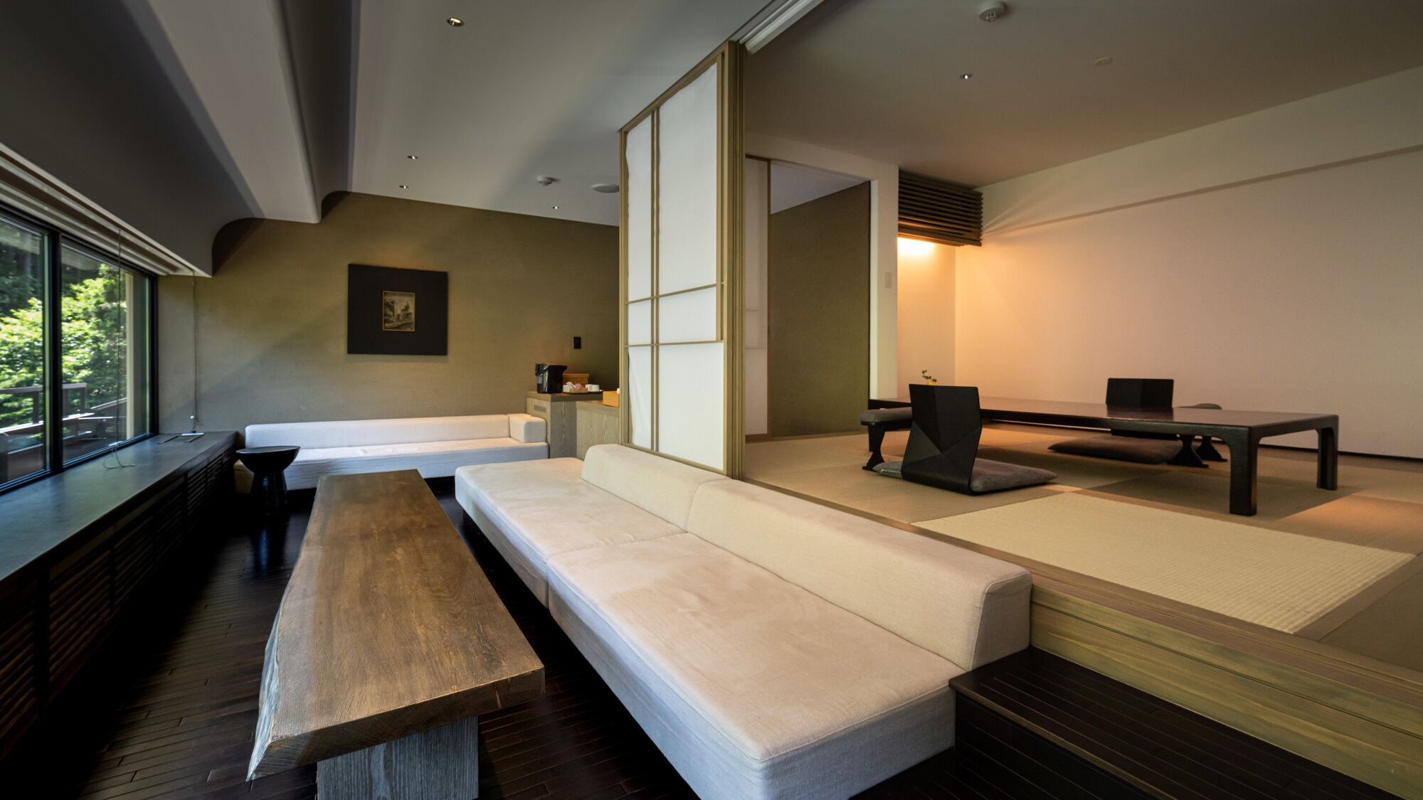 A modern room with a sofa, a bench, a table, and a view through large windows.