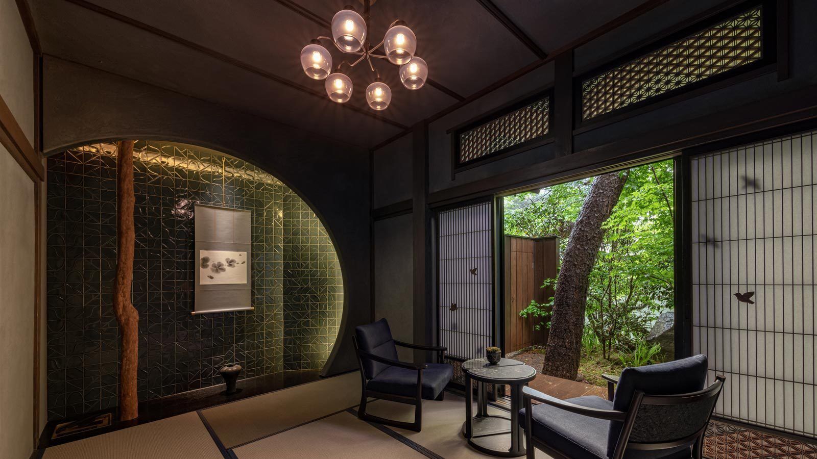 A traditional Japanese-style room with tatami flooring, a low table with chairs, a hanging light fixture, and a view of greenery outside.