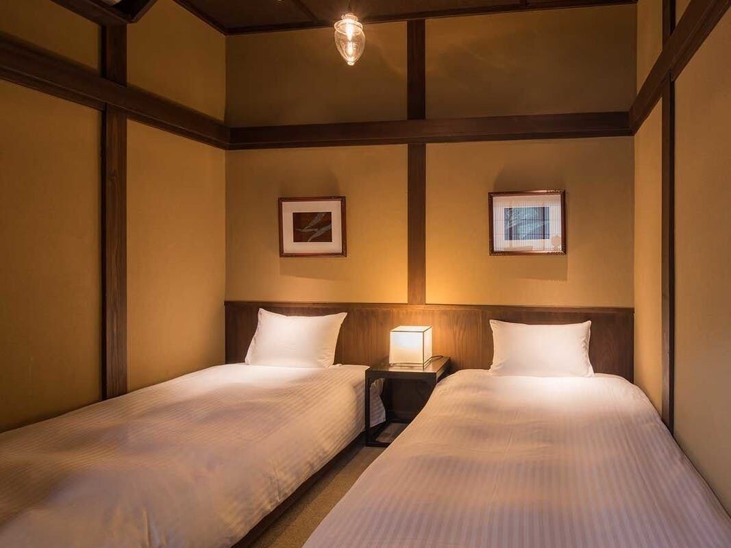 A hotel room with two beds, a nightstand with a lamp, and framed pictures on the wall.