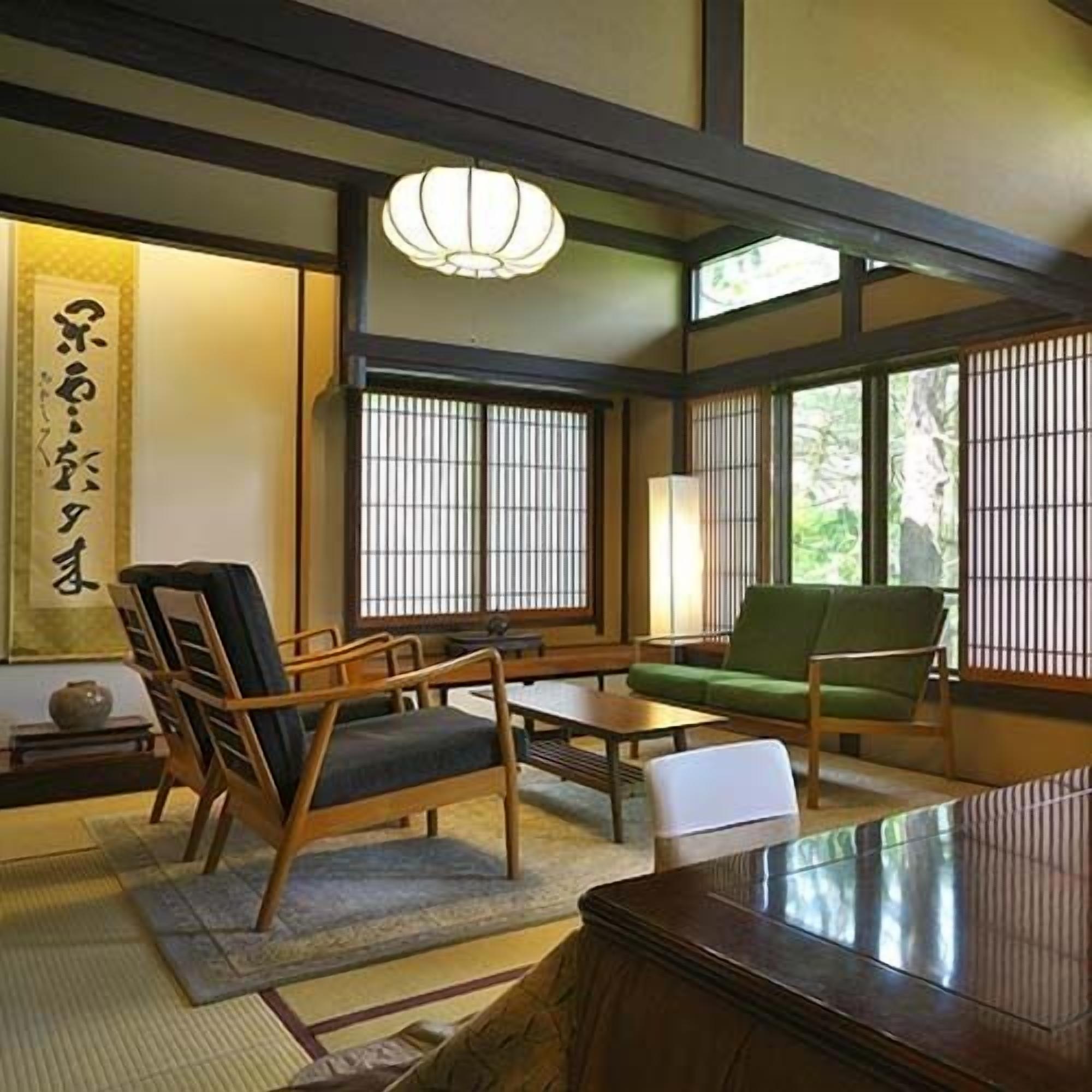 A traditional Japanese room with tatami flooring, a low table, a sofa, and a green chair.