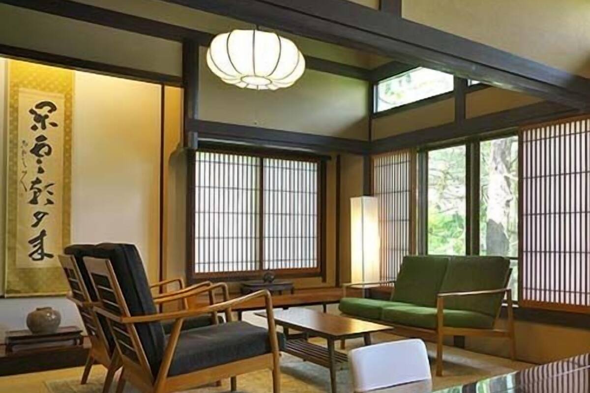 Une pièce de style japonais traditionnel, avec un sol recouvert de tatamis, une table basse, un canapé et un fauteuil vert.