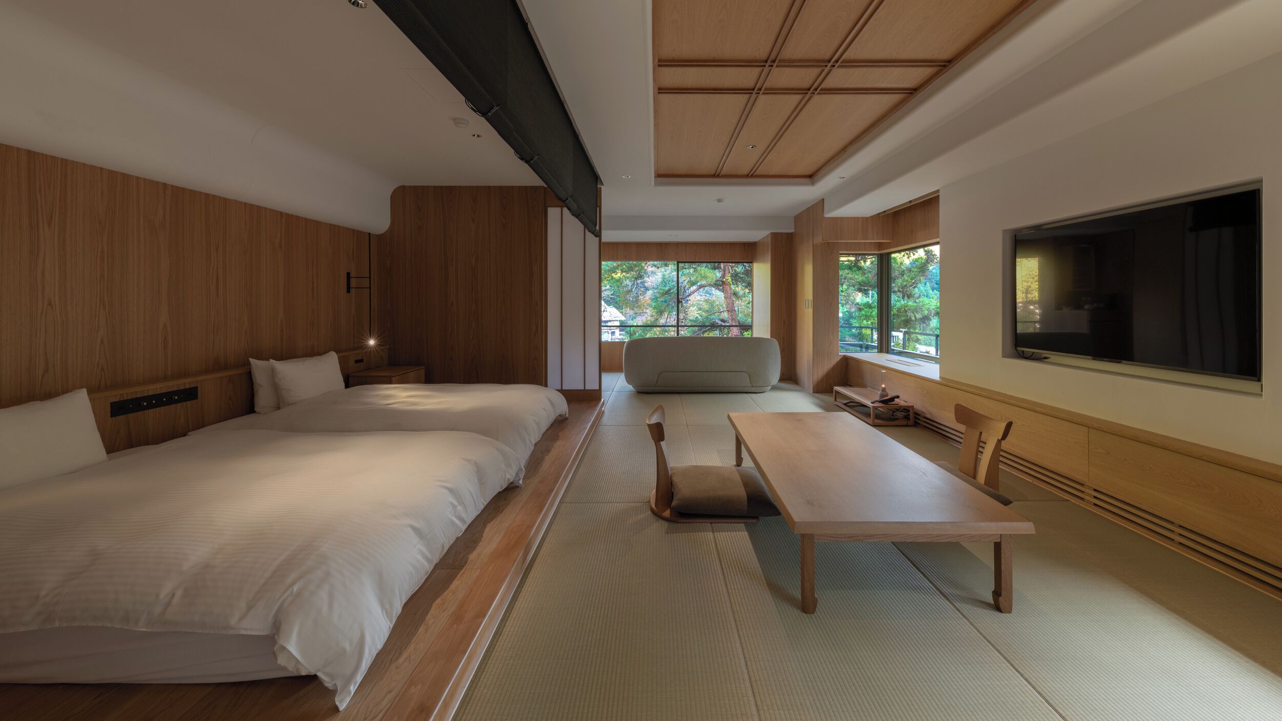 A modern hotel room with a large bed, a sofa, a dining table, and a TV.