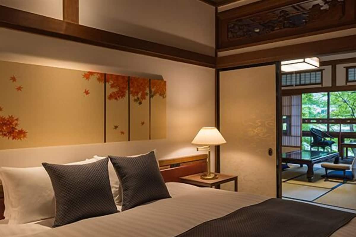 Una habitación de hotel con cama, almohadas, una mesita de noche con lámpara y vistas al exterior a través de una puerta corrediza.