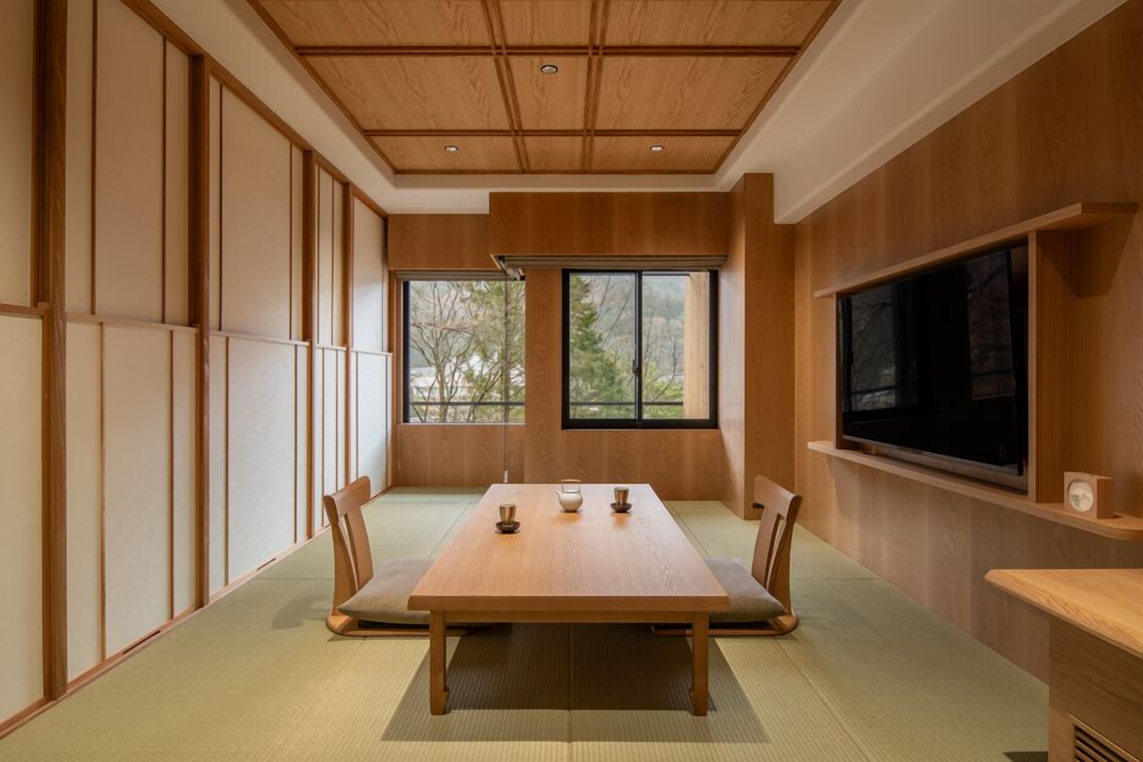 A traditional Japanese-style room with tatami flooring, a low table, and a television mounted on the wall.