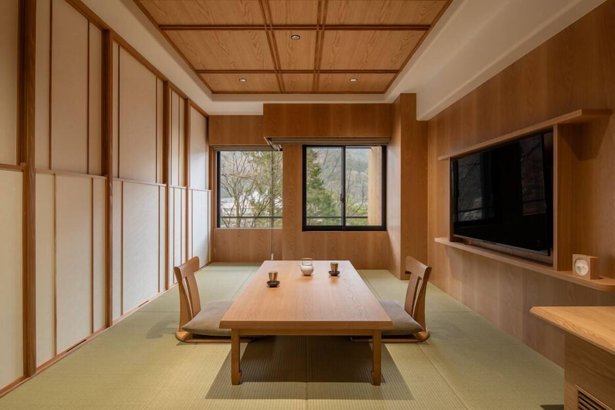 Une pièce de style japonais traditionnel, avec un sol recouvert de tatamis, une table basse et un téléviseur fixé au mur.