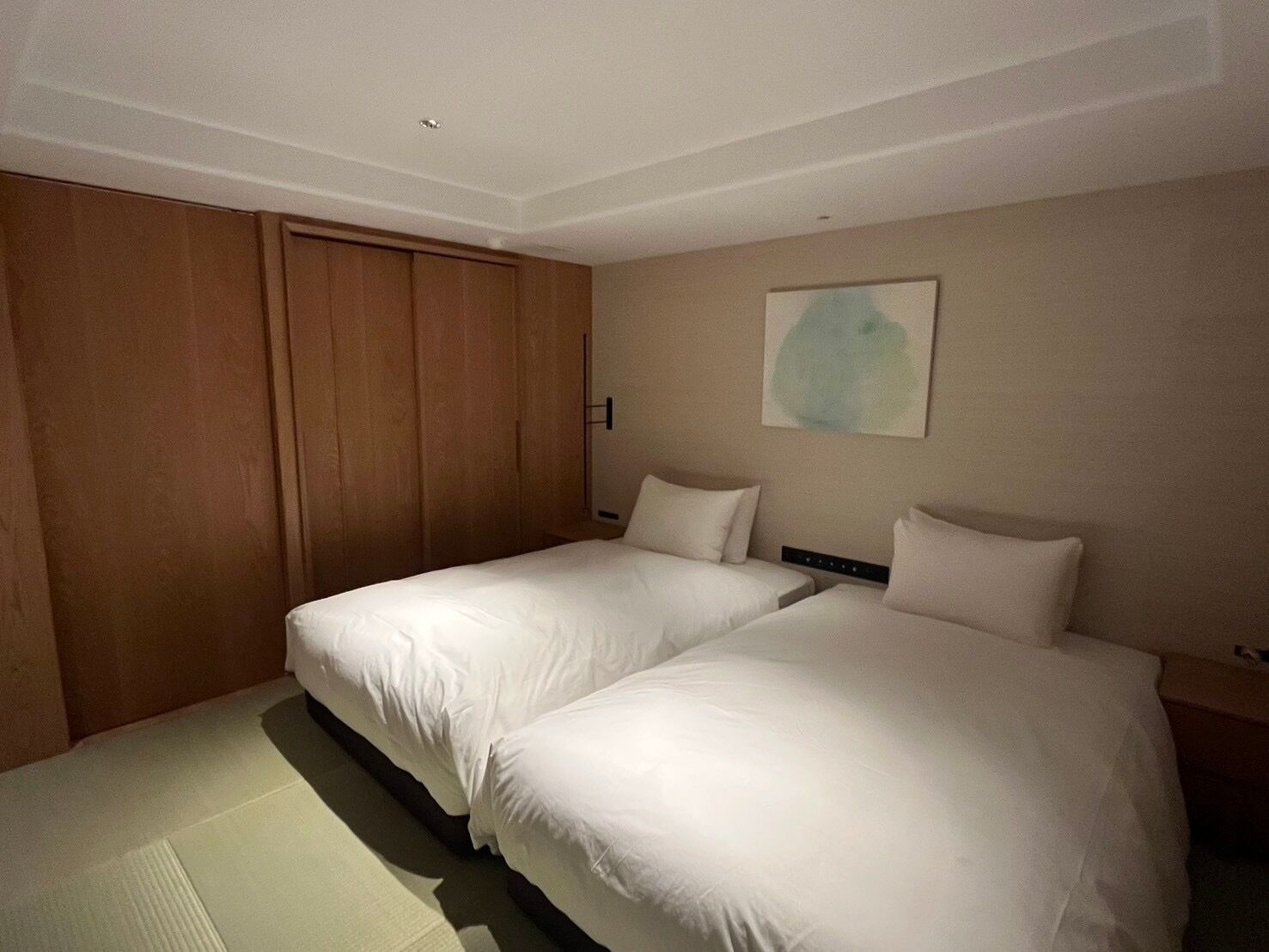 A hotel room with two beds, a wooden wardrobe, and a painting on the wall.