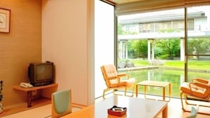 Quarto de hotel moderno com uma grande porta de vidro deslizante, uma mesa de madeira, duas cadeiras, uma televisão e uma pequena planta.
