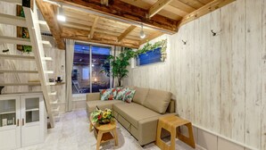 A modern living room with a sofa, a small wooden table with a floral arrangement, a staircase, and a large window with a view. - Orion Resort (Tokyo)