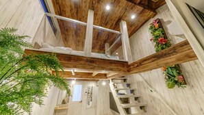 A wooden interior with a staircase, a bed, and a plant arrangement. - Orion Resort (Tokyo)