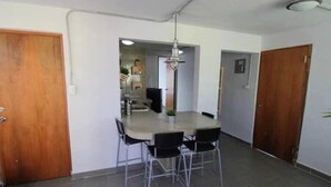 Un comedor con una mesa y sillas, una cocina al fondo y una puerta de madera.