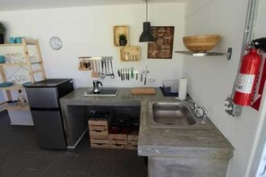 A compact kitchen with a built-in refrigerator, a sink, and various utensils hanging on the wall.