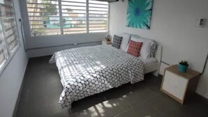 Un dormitorio con una cama, una ventana, una obra de arte en la pared y una mesita de noche con una planta.