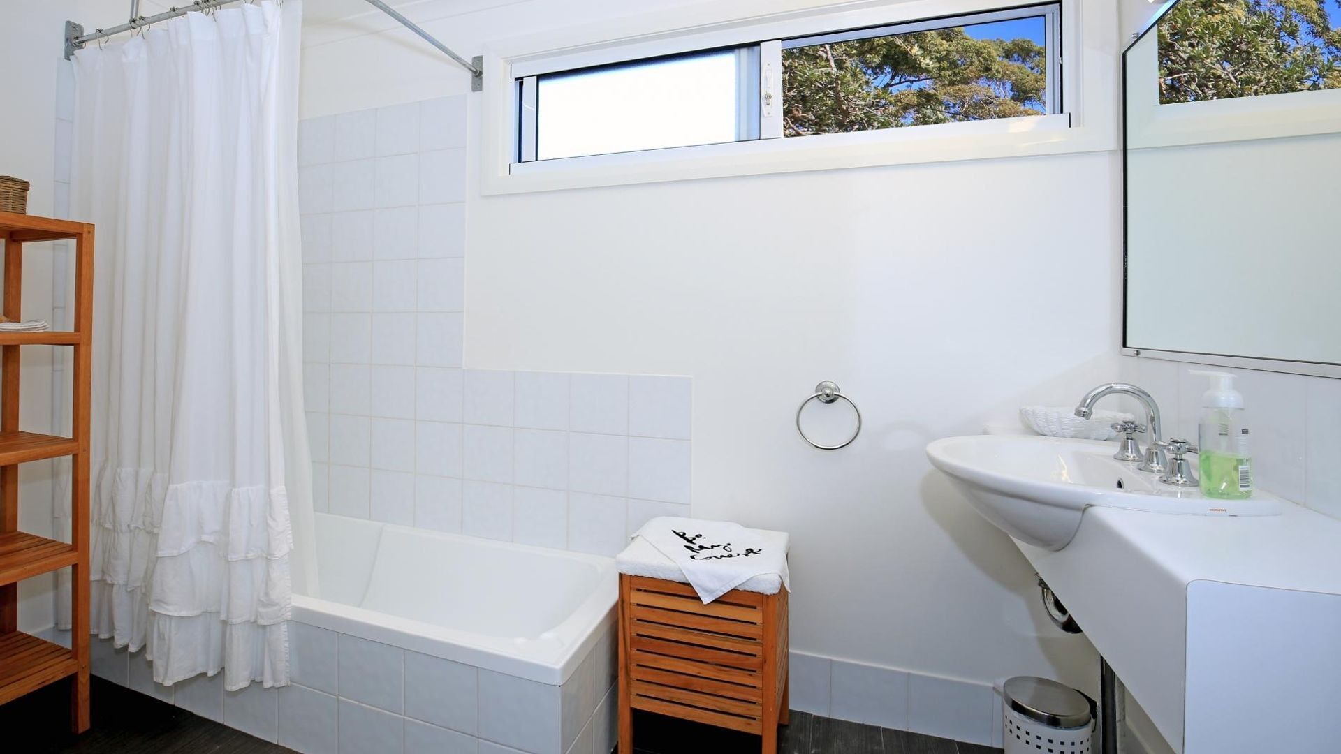 Un baño moderno con bañera, lavamanos y ventana con vistas a árboles.