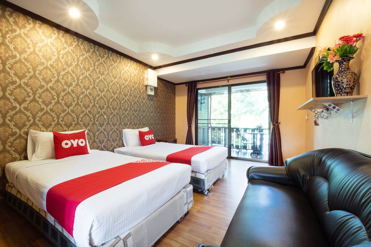 Hotelkamer met twee bedden, een sofa, een groot raam met uitzicht en een decoratieve vaas aan de muur.