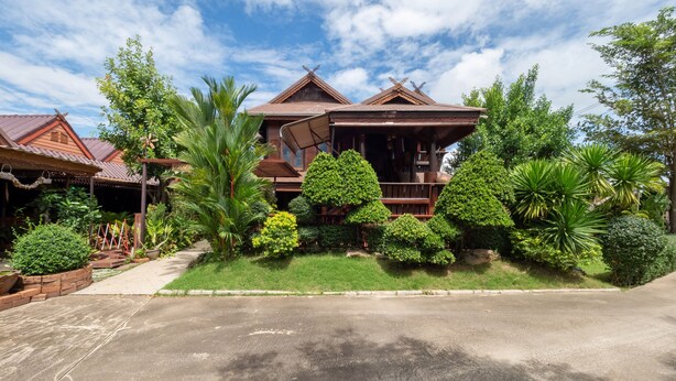 A traditional wooden house with a tiled roof, surrounded by lush greenery and a paved driveway. - OYO 1128 Ban Suan Meesakul Resort (Sattahip)