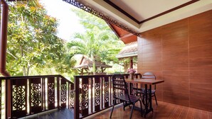 A balcony with a wooden table and chairs, surrounded by a decorative railing, overlooking a lush garden with various plants and a birdhouse. - OYO 1128 Ban Suan Meesakul Resort (Sattahip)