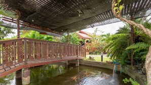 A bridge over a pond with koi fish, surrounded by lush greenery and a covered walkway. - OYO 1128 Ban Suan Meesakul Resort (Sattahip)