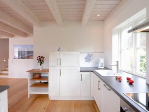 A modern kitchen with white cabinets, a wooden countertop, and a window with a view of greenery.