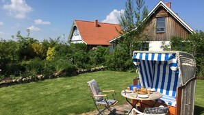 Une terrasse avec des meubles d’extérieur, un chemin de pierres et une maison avec un toit rouge en arrière-plan.