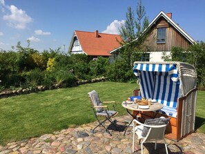 Eine Terrasse mit Gartenmöbeln, ein Steinweg und ein Haus mit rotem Dach im Hintergrund.