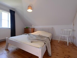 Un dormitorio con cama, cómoda, silla y ventana con cortinas.