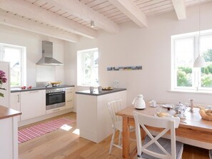 Una cocina moderna con armarios blancos, una isla central y un comedor con mesa y sillas de madera.