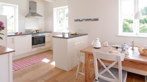 Une cuisine moderne avec des meubles blancs, un îlot central et un coin repas comprenant une table et des chaises en bois.