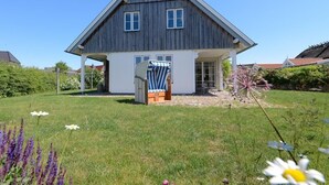 Une maison à deux étages, dotée d’un toit en pente, d’un porche à l’avant et d’un petit jardin fleuri.