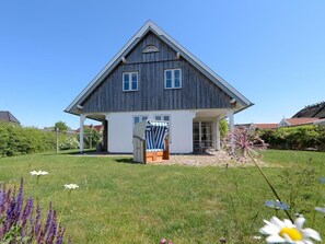 Ein zweistöckiges Haus mit geneigtem Dach, einer Veranda und einem kleinen Garten mit Blumen.