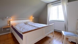 Une chambre à coucher avec un lit, des tables de chevet, une fenêtre avec des rideaux et une chaise.