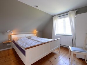 Ein Schlafzimmer mit Bett, Nachttischen, einem Fenster mit Vorhängen und einem Sessel.
