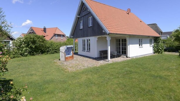 Une maison à deux étages, avec un toit recouvert de tuiles rouges, une véranda et un petit jardin.