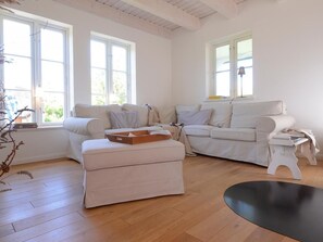 Un salon avec deux canapés, une table basse et une petite table blanche. De grandes fenêtres laissent entrer la lumière naturelle.
