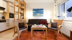 A cozy living area with a sofa, two wicker chairs, a coffee table, and a kitchen in the background. - Urlauberdorf 40b, Deutschland (Ostseebad Boltenhagen)