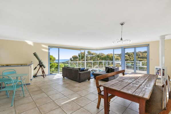 A spacious living area with a large window, a telescope, and a wooden table.