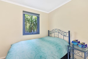 A bedroom with a bed, a window with a view of palm trees, and a small table with a fish decoration.
