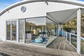 A modern building with large glass windows, a wooden deck, and a visible interior with furniture. - Caprica (Fairhaven)
