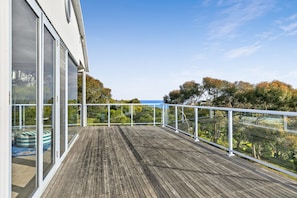 A wooden deck with glass railings overlooking a landscape with trees and a view of the sea.