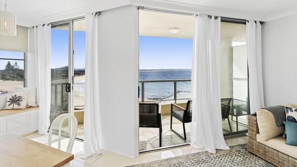 A modern room with a balcony overlooking a beach, a dining area, and a seating area with a view. - Beachpoint Unit 503 (Forster)