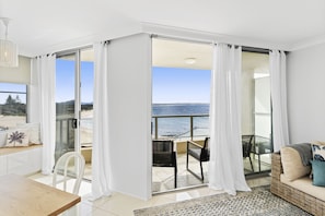 Una habitación moderna con balcón que da a una playa, zona de comedor y área de estar con vistas.