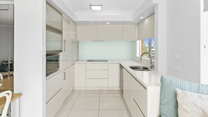A modern kitchen with white cabinetry, a stainless steel sink, and a window with a view of the city. - Beachpoint Unit 503 (Forster)