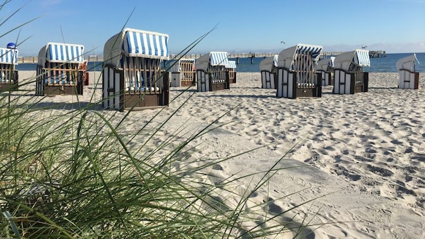 Strandhutten met strepenpatroon luifels, een zandstrand en een pier op de achtergrond.