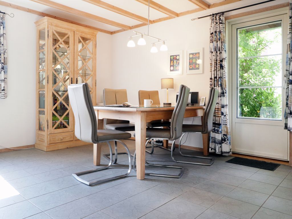 Un comedor con una mesa y sillas de madera, un armario con puertas de cristal y una ventana con cortinas.