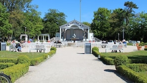 Een gazebo met een podium, omringd door banken en paden in een park.